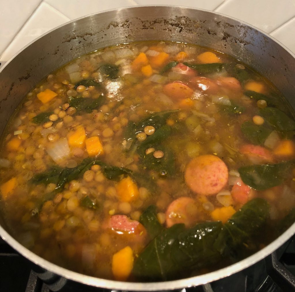 Lentil soup with sweet potato, spinach and sausage in a pot on the stove