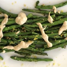 green beans on a white plate drizzled with a tahini sauce and lemon zest