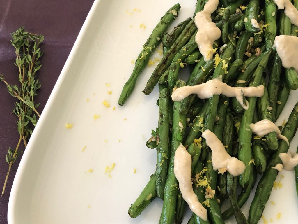 green beans on a white plate with tahini sauce