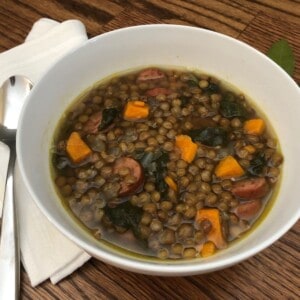 Lentil Soup with Sausage in a white bowl with a napkin and a spoon.