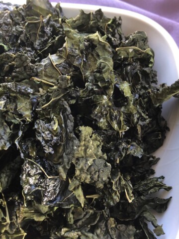 Roasted kale chips in a white bowl with a purple napkin