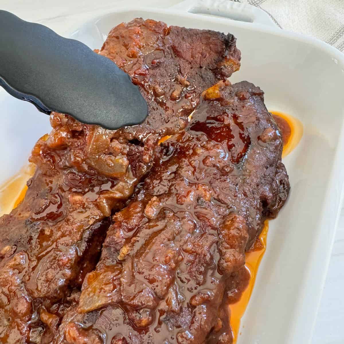 Boneless Beef Ribs cooked in a casserole and held up by tongs. 