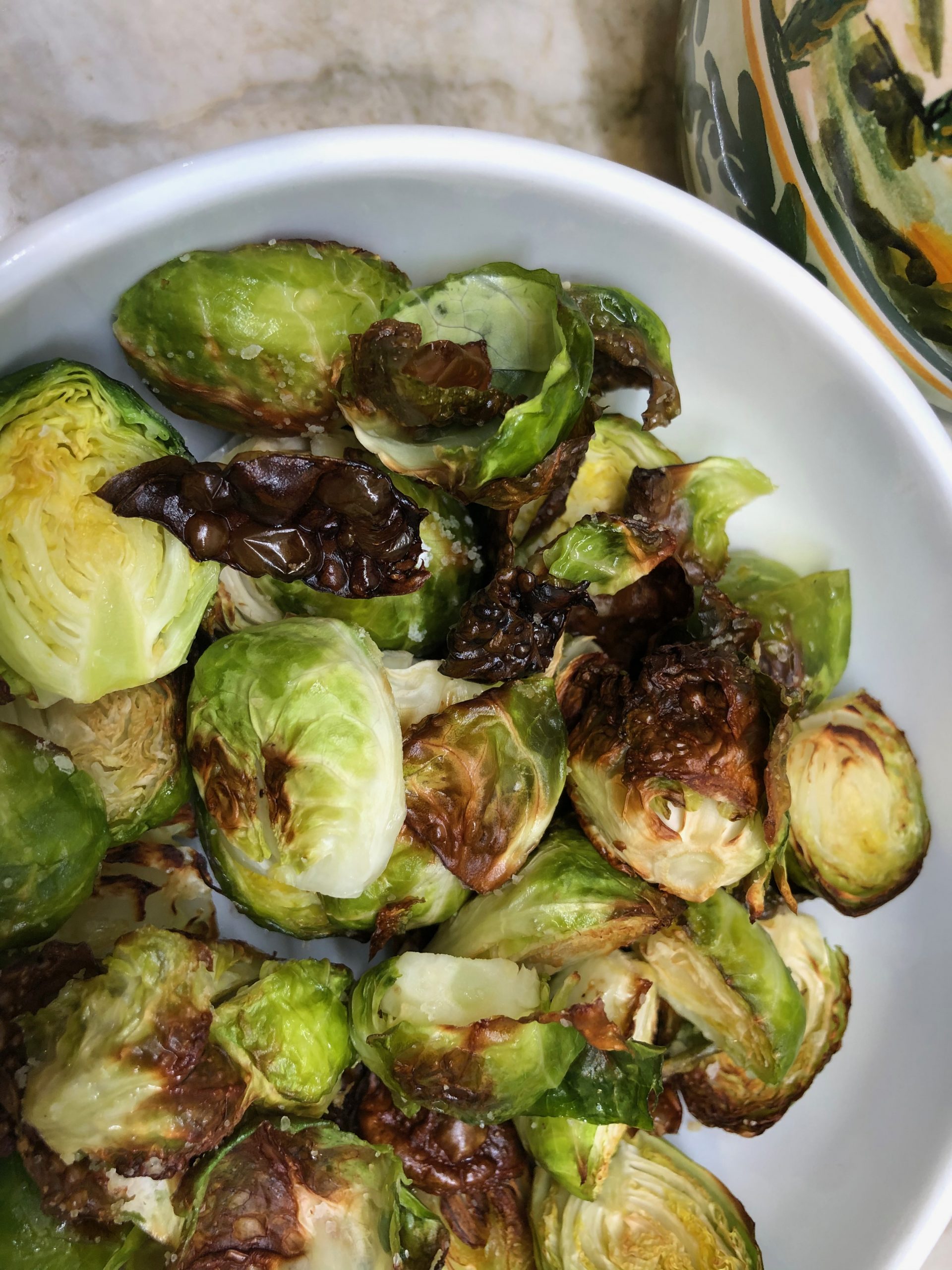 a bowl of roasted brussel sprouts with an olive oil cruet next to it