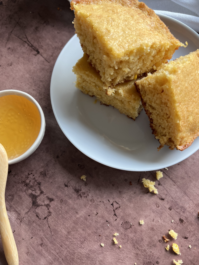 cornbread on a plate with a bowl of honey on the side