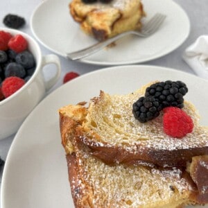 two servings of overnight french toast casserole on white plates and served with mixed berries.