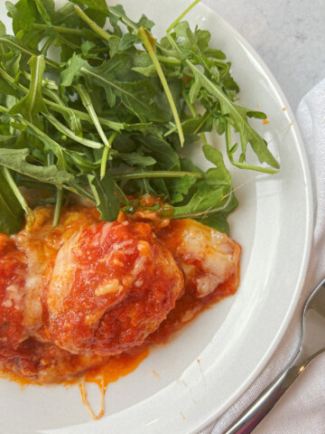 a white plate filled with cheesy chicken meatballs and arugula.