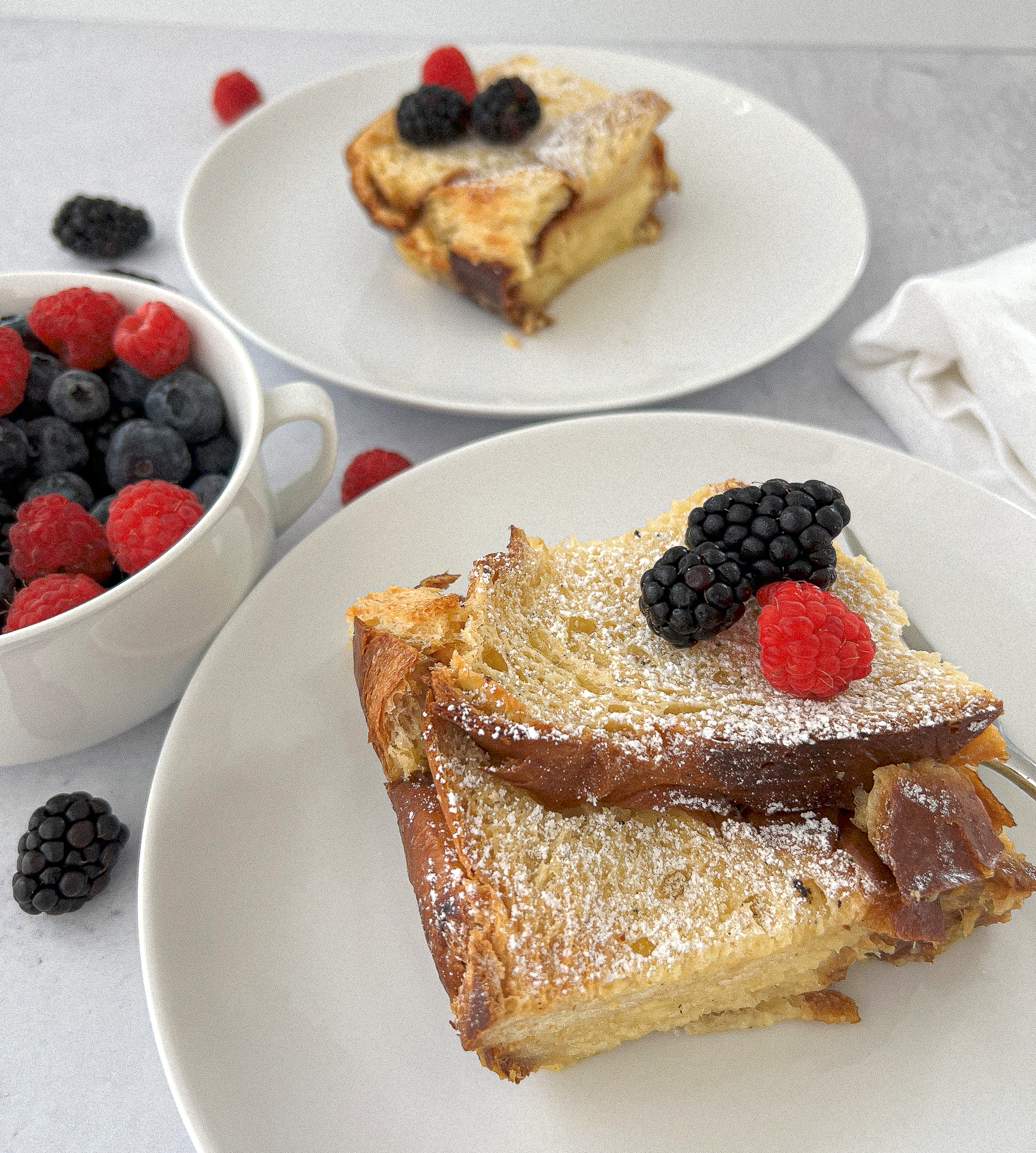 two servings of overnight french toast casserole on white plates and served with mixed berries.