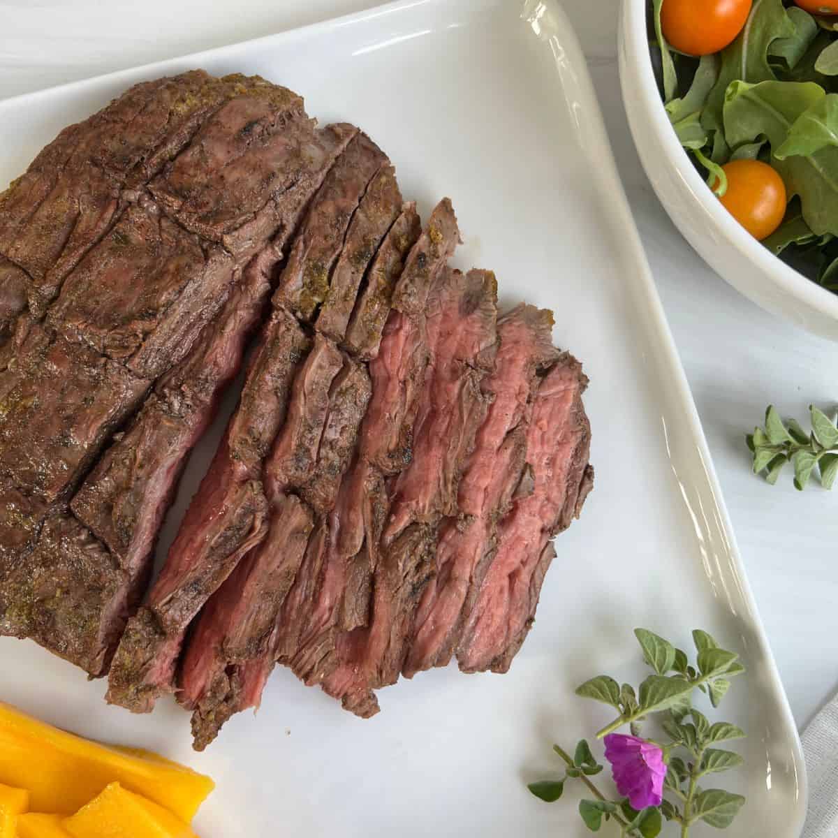 flank steak on a white plate with salad and mango slices.