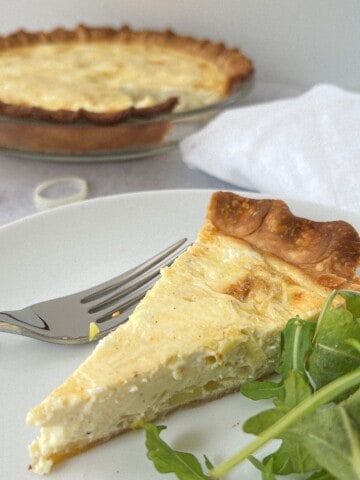 Leek and Goat Cheese Quiche Recipe on a white plate with a fork and arugula