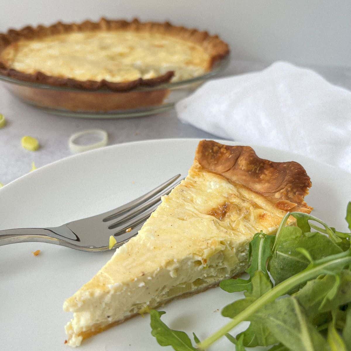 Leek and Goat Cheese Quiche Recipe on a white plate with a fork and arugula
