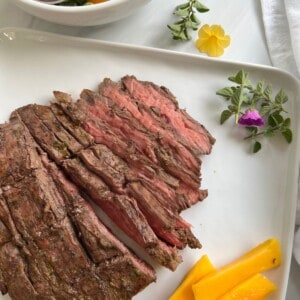 flank steak on a white plate with salad and mango slices.