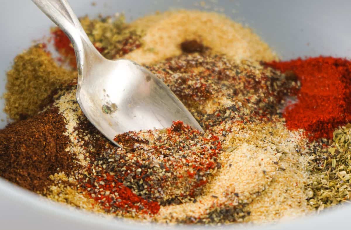 all the ingredients for Authentic Homemade Taco Seasoning Recipe in a white bowl with a spoon