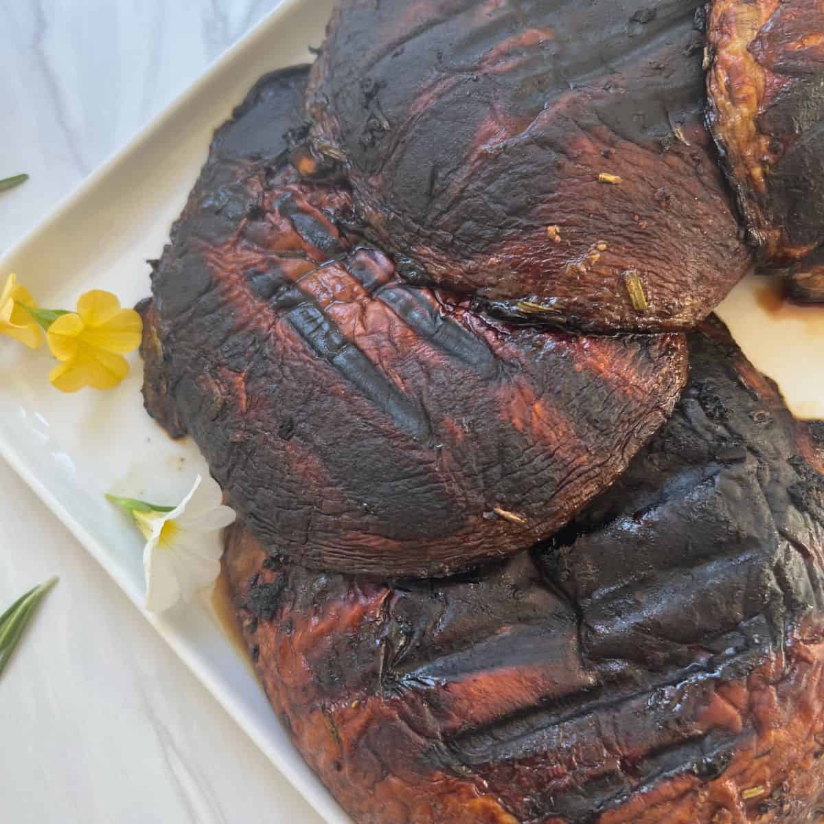 grilled marinated portobello mushrooms on a white plate with rosemary and flowers