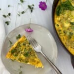 A slice of smoked salmon frittata on a white plate with a fork.