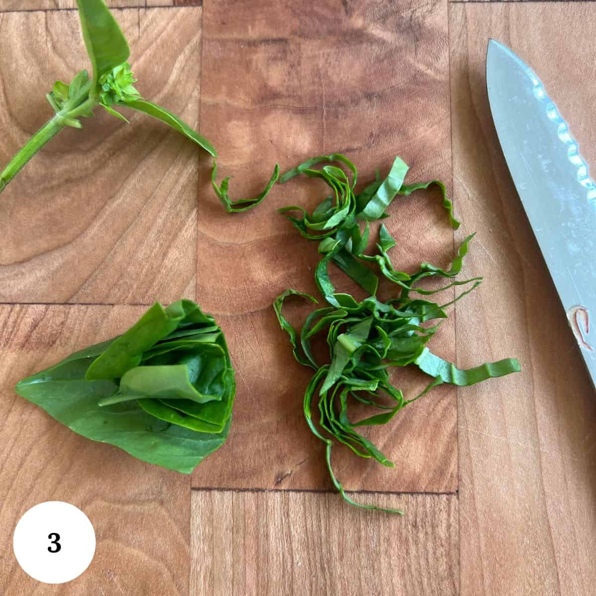A wooden cutting board with sliced green basil leaves, a chef's knife, a basil stem, and a rolled stack of basil leaves-perfect prep for your Nectarine Salad. A white circle with the number 3 appears in the bottom left corner.