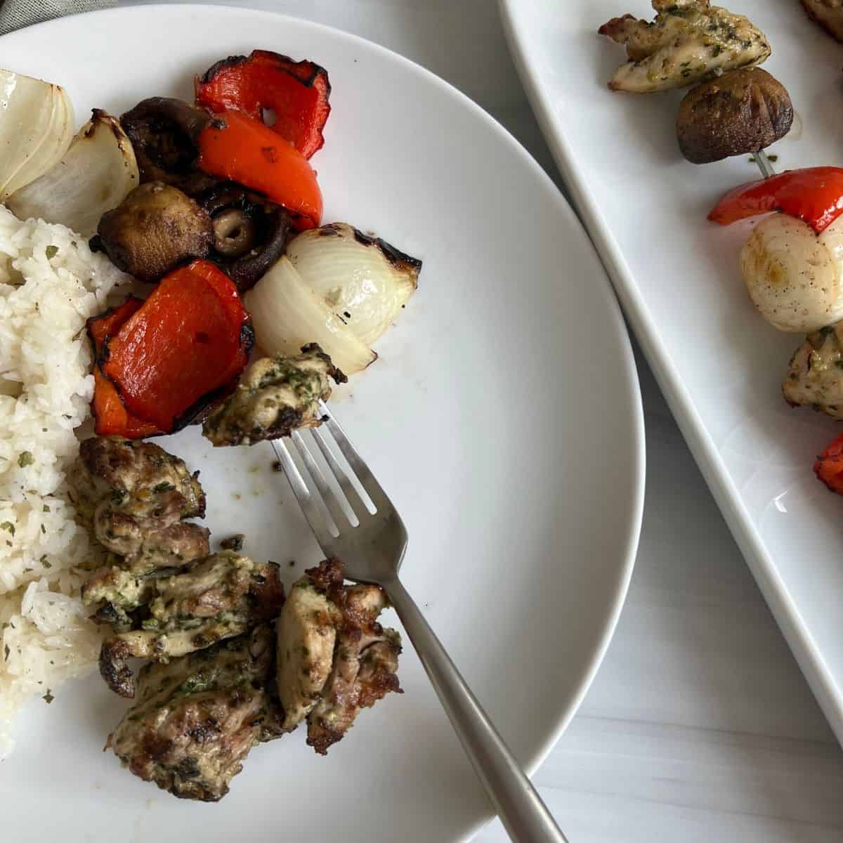 grilled chicken kabob on a white plate with a fork and rice.