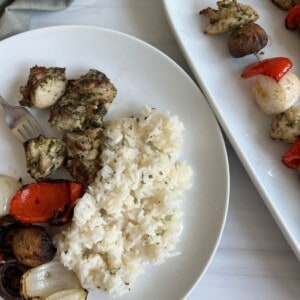 Grilled Chicken Kabobs on a white plate with a pesto marinade and rice.