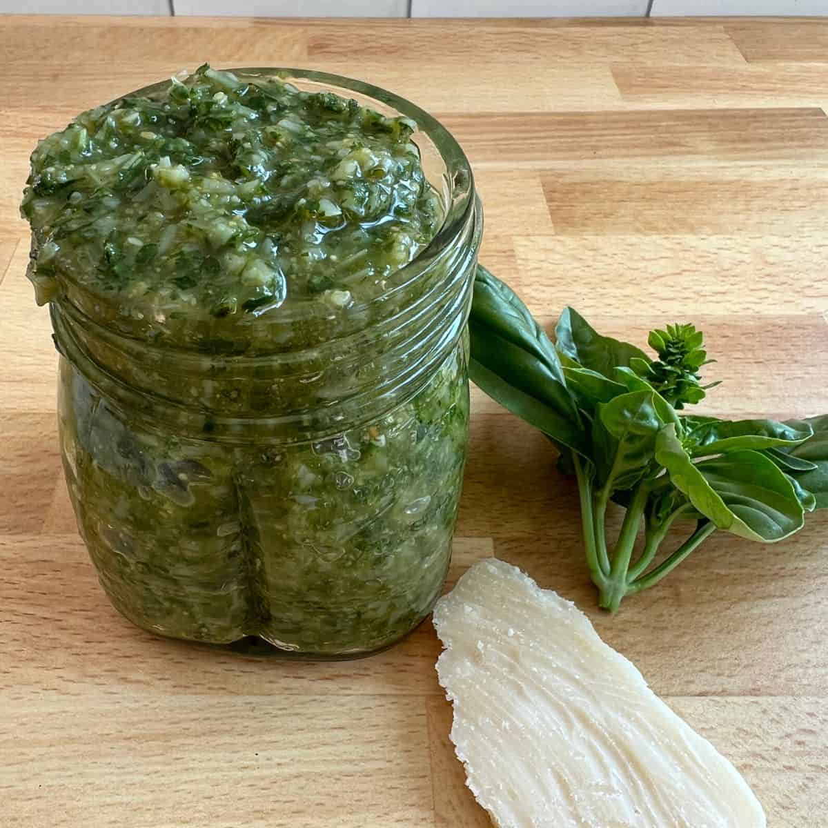 Homemade basil pesto in a jar on the counter with parmesan cheese. 