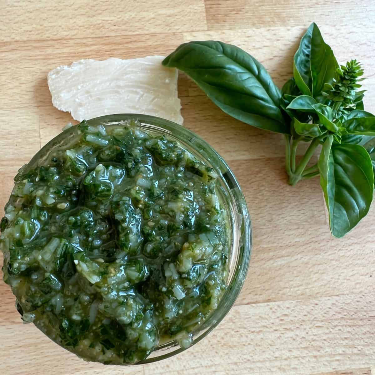 Homemade basil pesto in a small jar on a counter. 