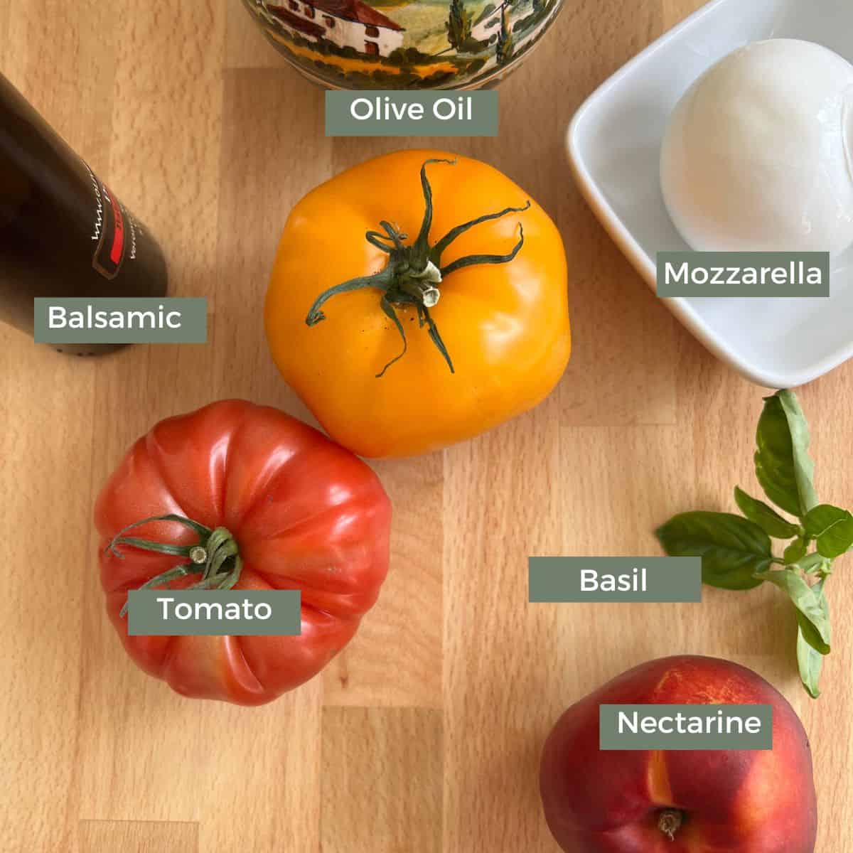 ingredients for a tomato nectarine mozzarella salad recipe on a cutting board which includes nectarines, tomatoes, mozzarella, and basil.