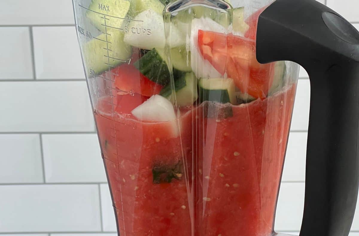 adding cucumber and onion to the tomatoes in the blender