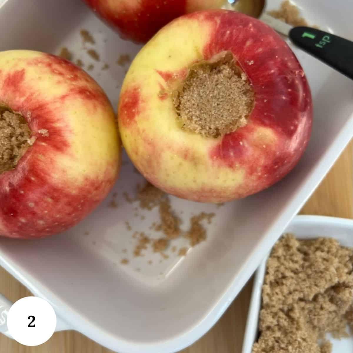 cored apples sitting in a baking dish with brown sugar in the core