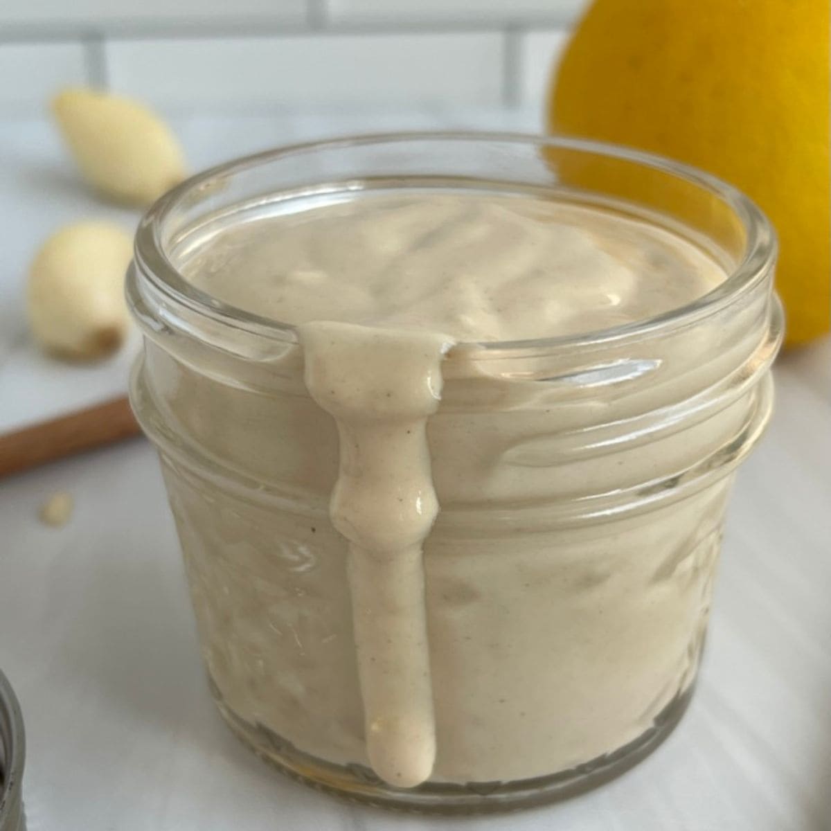 Lemon Garlic Tahini Sauce in a small jar with some of the sauce pouring out. 