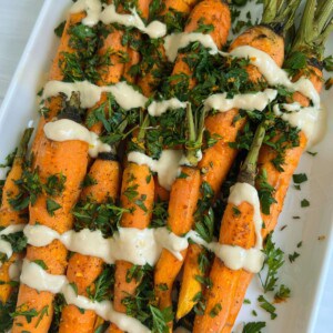 Roasted carrots with tahini sauce and a gremolata on a white platter.