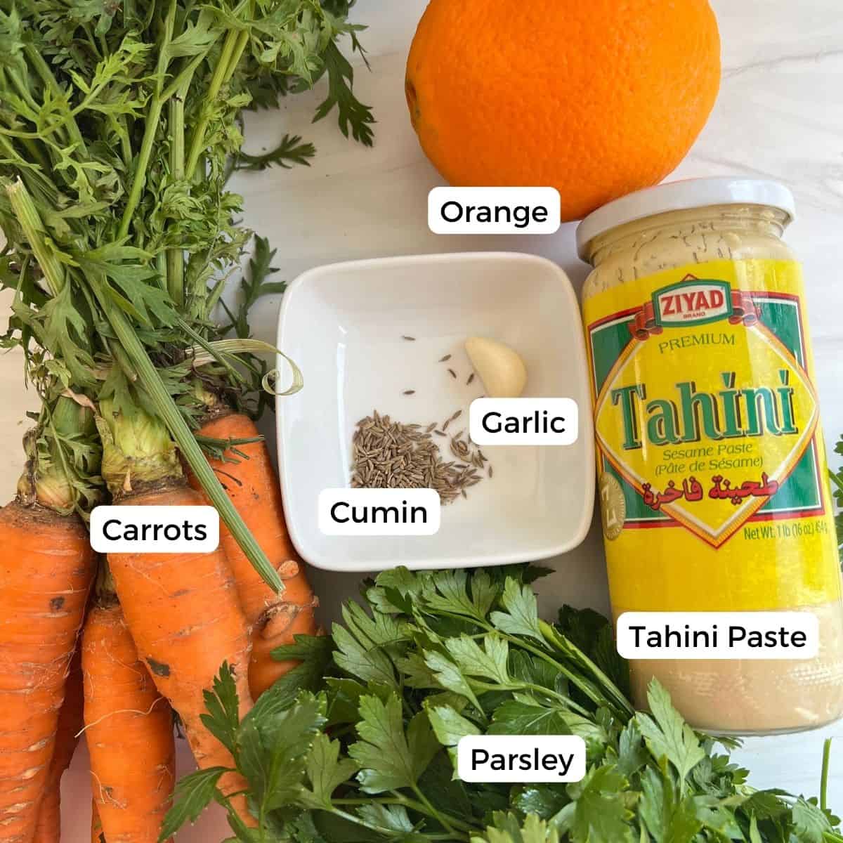 ingredients for roasted carrots with gremolata include orange, cumin, garlic, carrots, parsley, and a tahini sauce.