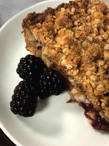 A slice of Unique Apple Cranberry Torte Dessert Recipe on a white plate with blackberries.