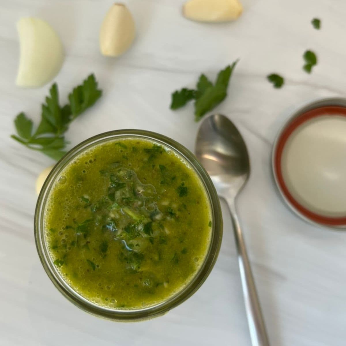 Easy Authentic Chimichurri Sauce Recipe top view with a spoon, parsley and garlic
