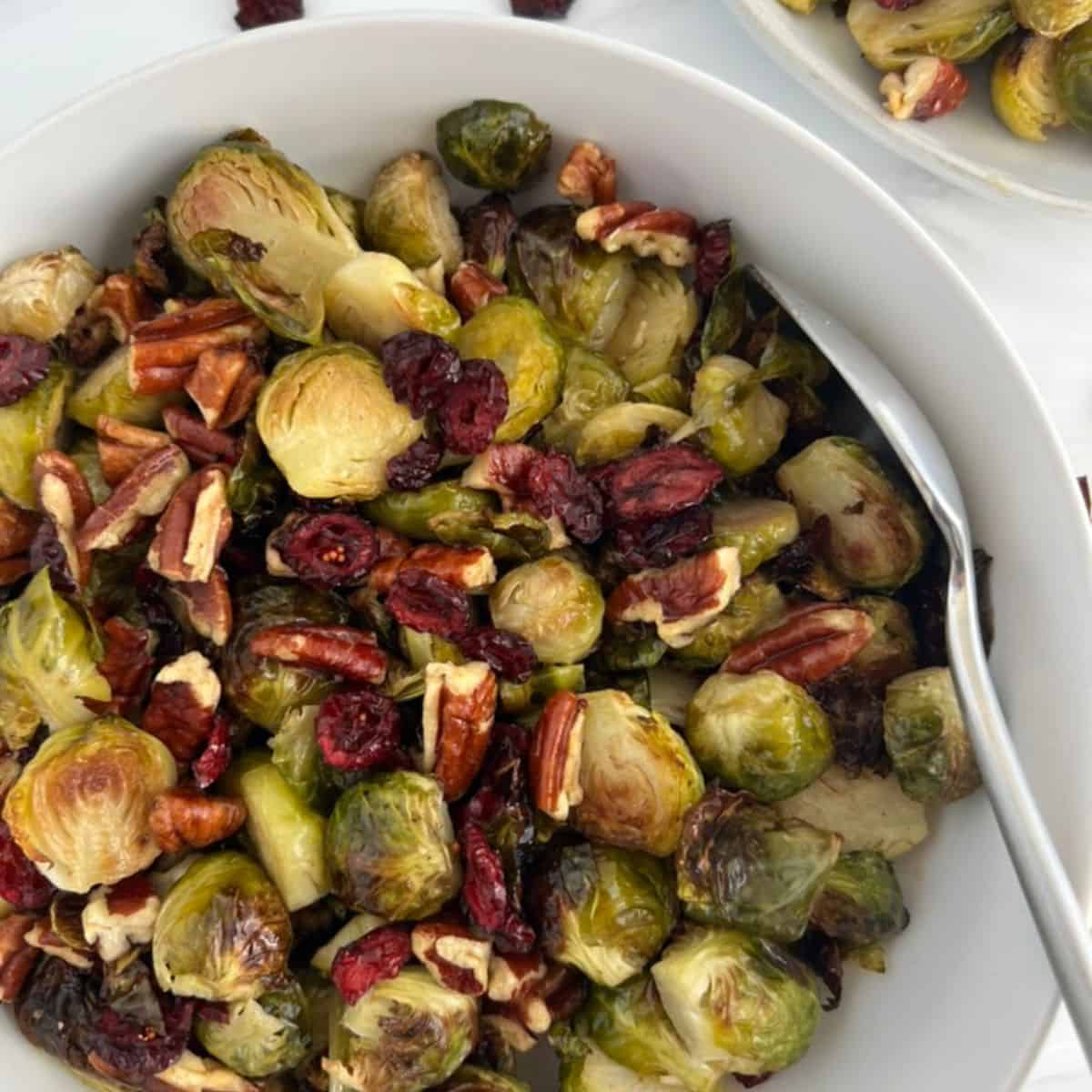 a bowl of Roasted Brussels Sprouts With Pecans And Cranberries, With A Maple Dijon Vinaigrette with a spoon