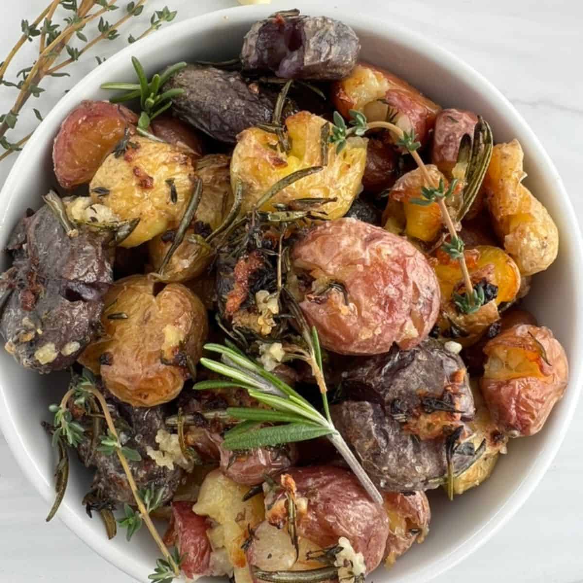 Roasted smashed potatoes with garlic, thyme, and rosemary in a white bowl.