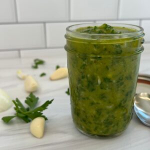 featured image for authentic chimichurri sauce recipe in a mason jar with garlic on the side.