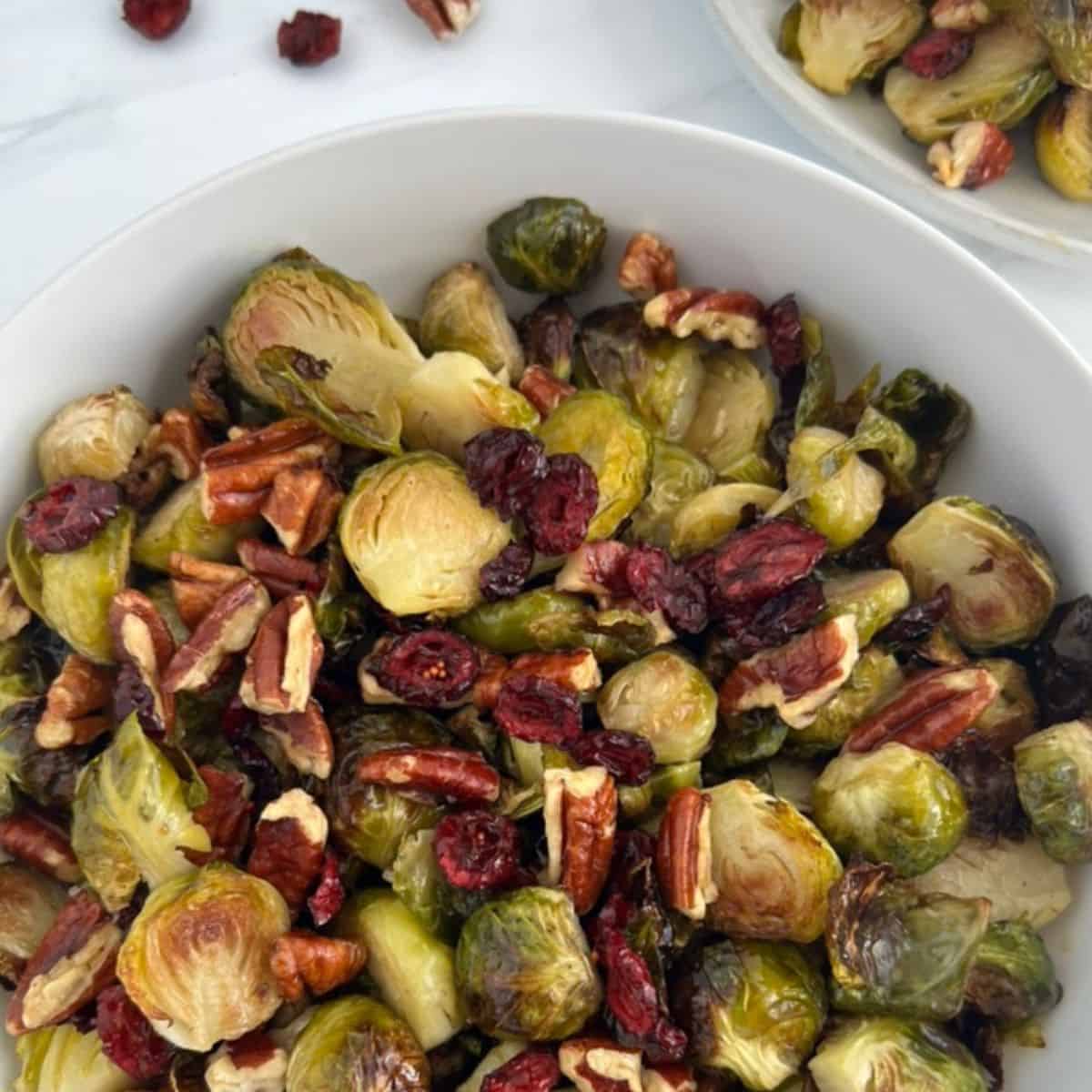 Roasted Brussels Sprouts With Pecans And Cranberries, With A Maple Dijon Vinaigrette in a white bowl.