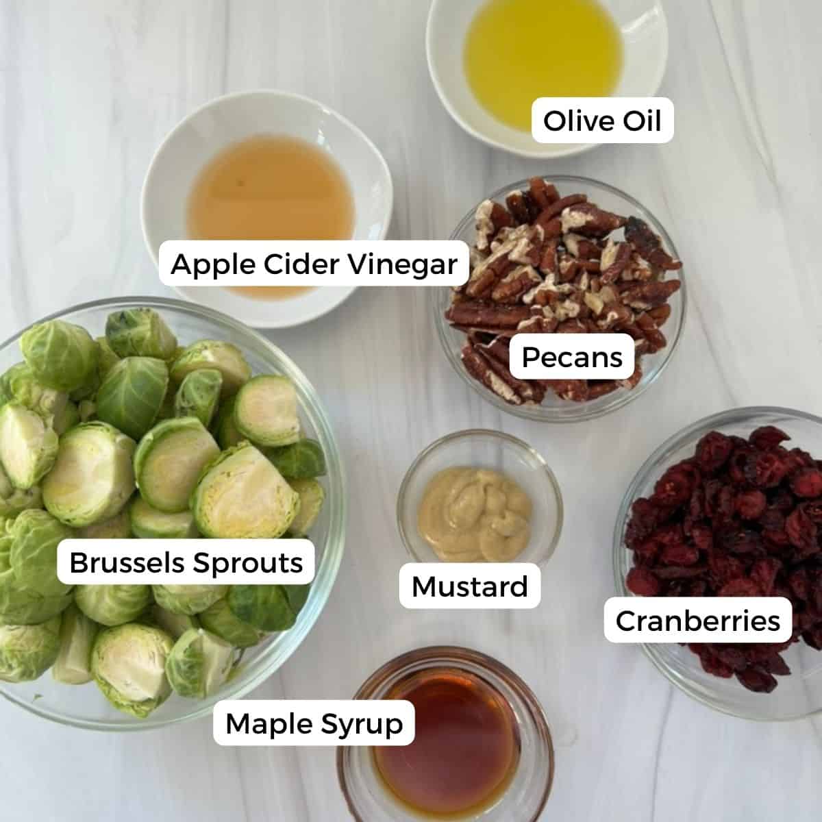 ingredients for Roasted Brussels Sprouts With Pecans And Cranberries, With A Maple Dijon Vinaigrette include olive oil, apple cider vinegar, brussels, pecans, mustard, maple syrup, and cranberries.