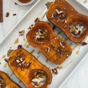 honeynut squash on a white platter with butter, cinnamon, pecans, and maple syrup.