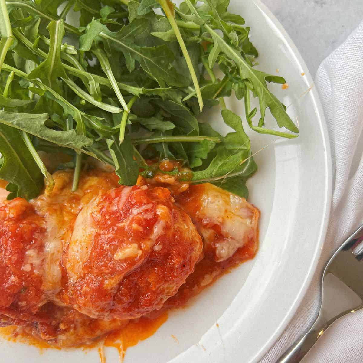 chicken parm meatballs on a white plate with arugula and a fork