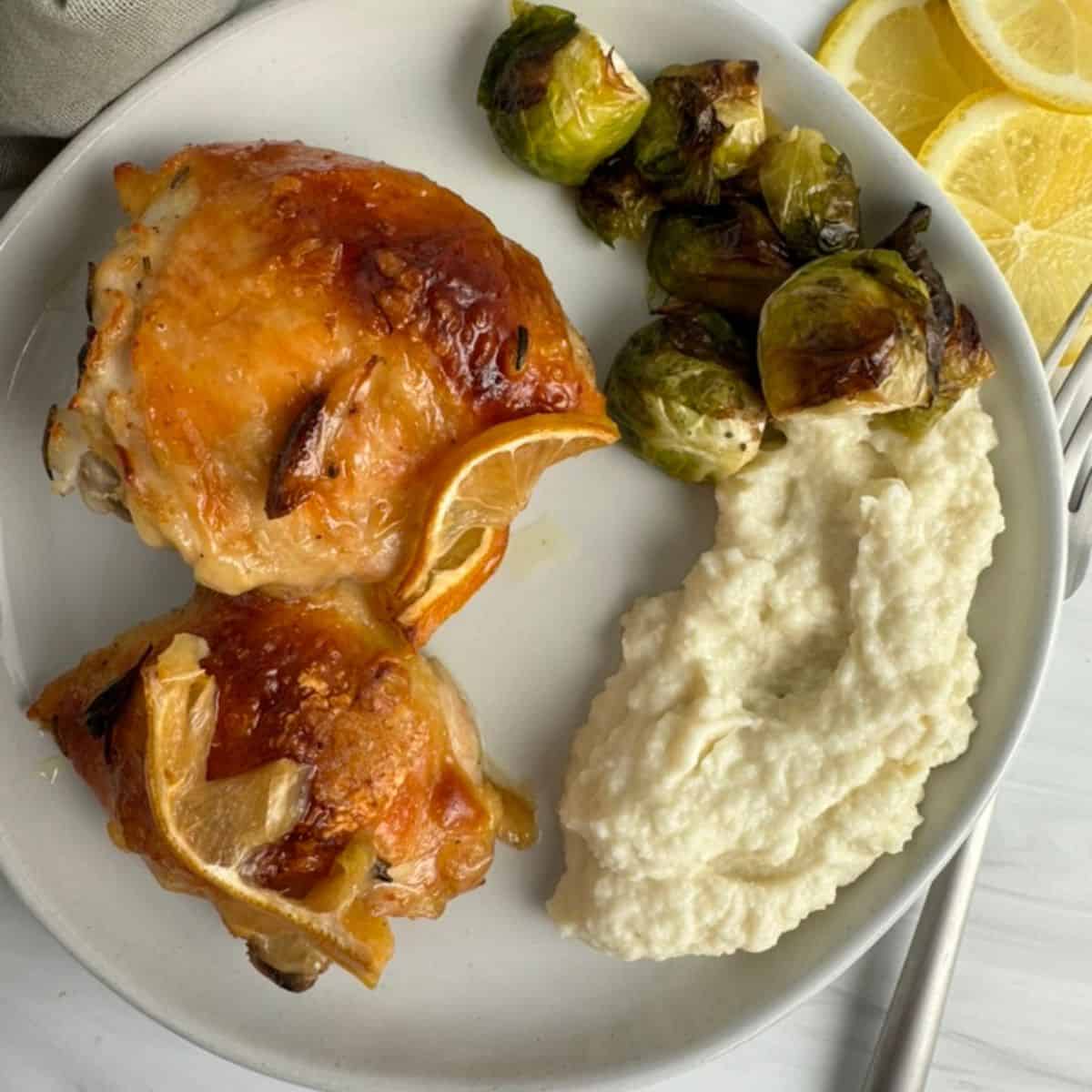 baked chicken thighs on a white plate with brussel sprouts and mashed potatoes. 