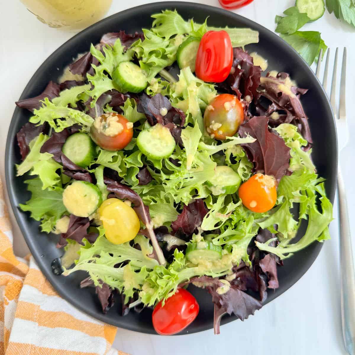 Salad with the dressing on a black plate and a fork. 