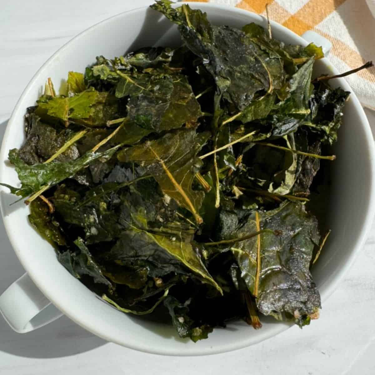 A white bowl filled with roasted kale chips and a yellow towel on the side. 