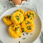 Egg bites piled on a white plate with chives scattered around.