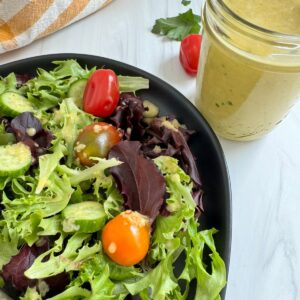 Zesty Apple Cider Vinaigrette Salad Dressing on lettuce which is sitting on a black plate.