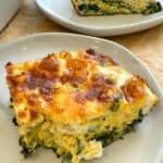 Baked spinach feta and egg casserole slice on a white plate.