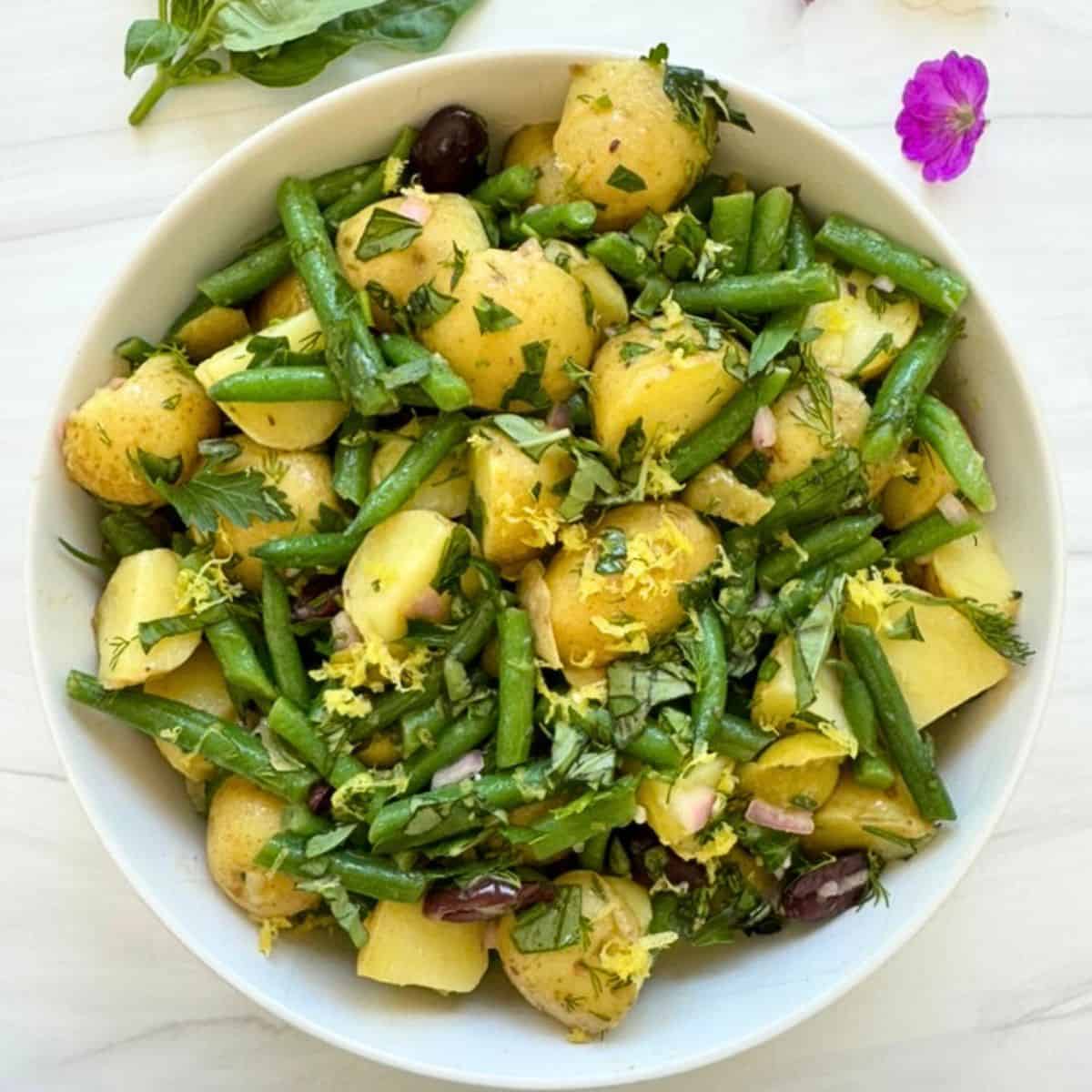 Gluten-free potato salad with green beans, herbs, and olives in a white bowl. 