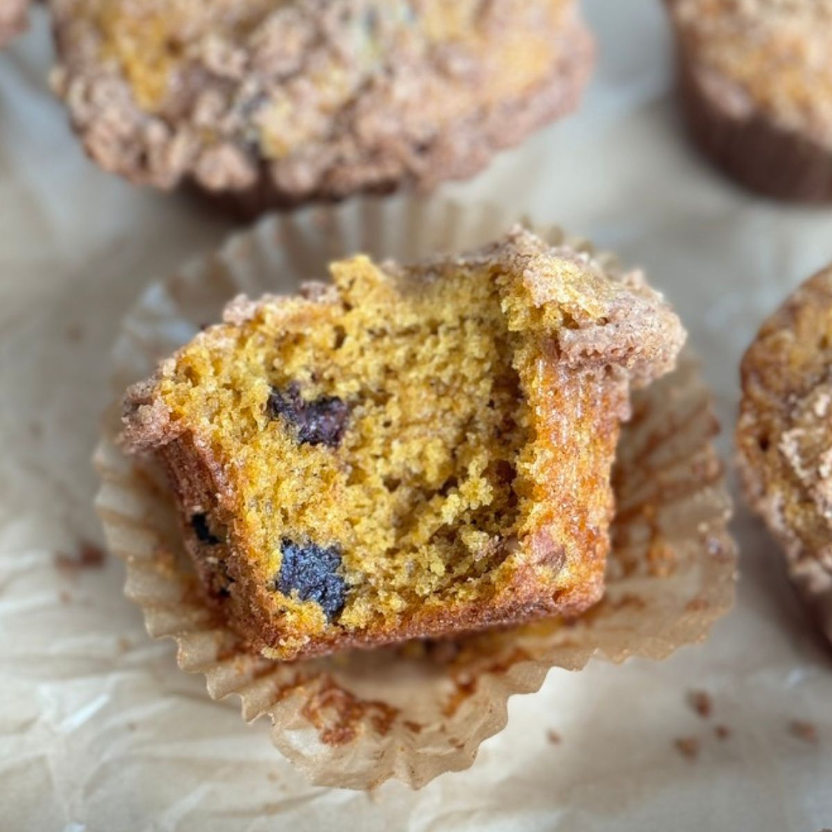 Gluten-free pumpkin muffin that has a bite out of it and is sitting in the paper wrapper. 