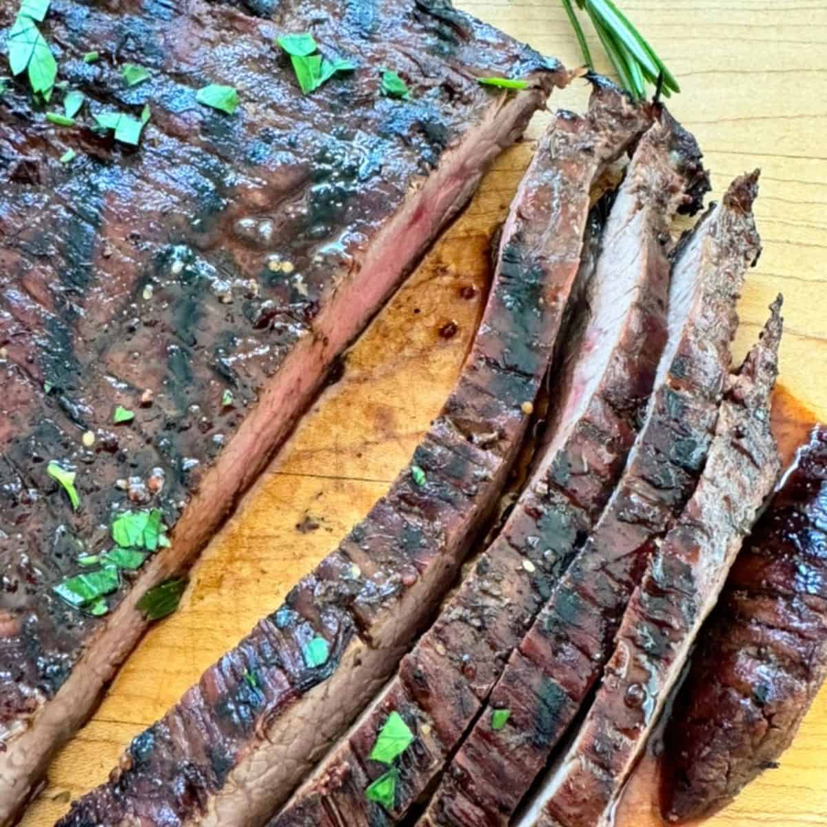 grilled flank steak marinaded in a balsamic vinaigrette and cut on a cutting board. 