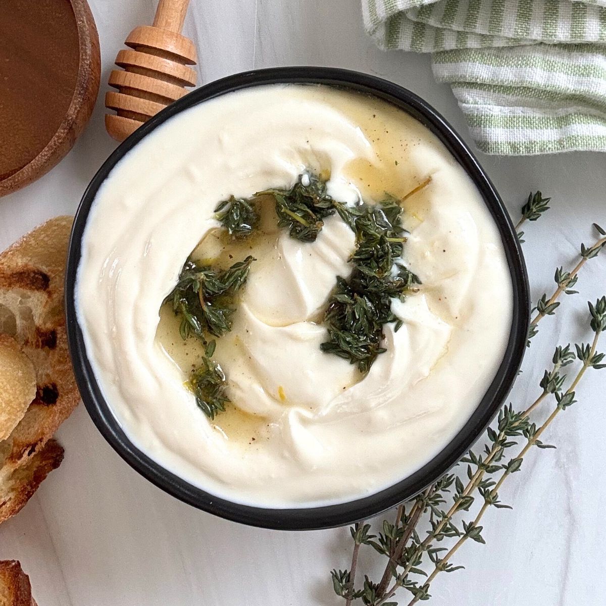 Whipped ricotta dip in a black bowl with lemon, thyme, honey, and spices on top. 