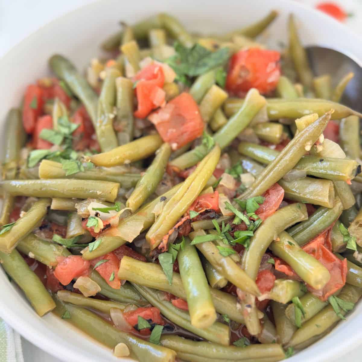 Greek green beans in a tomato sauce in a white bowl with a spoon. 