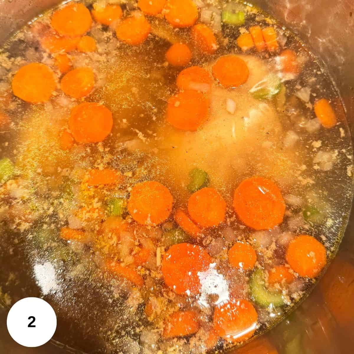 Adding the broth, chicken, and spices to the carrot mixture in the stockpot. 